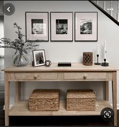 a wooden table with baskets underneath it and pictures on the wall behind it in front of stairs