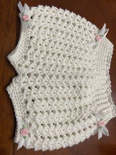 a white crocheted blanket with pink flowers on the edge and two bows at the bottom