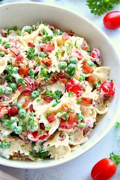 a bowl filled with pasta and vegetables on top of a white table next to tomatoes