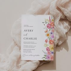 a wedding card with flowers on it sitting on top of a pile of white fabric