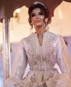 a woman in a white dress and tiara standing next to a gazebo with her hands on her hips