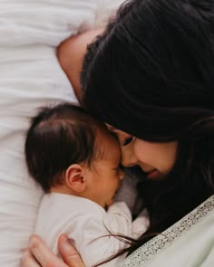 a woman holding a baby in her arms while laying on top of a white bed