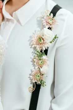 a woman wearing a white shirt and black tie with flowers on it's lapel