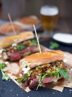 two sandwiches with meat, lettuce and other toppings sit on wax paper