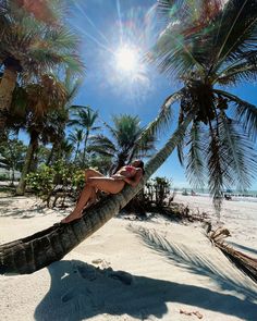 a woman laying in a hammock on the beach with palm trees around her