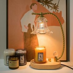 a candle and some jars are on a table next to a painting with palm trees in the background