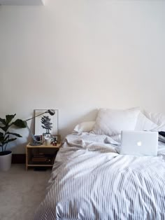 a laptop computer sitting on top of a bed next to a plant in a vase