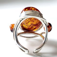 The Handcrafted Large Amber ring is just stunning. The Large Oval Amber Ring is a stunning piece of jewelry featuring an oval-shaped amber gemstone as its centerpiece. The amber gemstone, known for its warm and rich color, adds a touch of elegance and natural beauty to the ring. Surrounding the amber gemstone, on each side, are two round beads that complement the main stone and add a balanced and symmetrical look to the design. The combination of the oval amber gemstone and the round beads creat Oval Citrine Amber Rings, Oval Amber Citrine Ring, Amber Citrine Oval Ring, Modern Amber Oval Ring, Elegant Oval Amber Rings, Elegant Amber Oval Rings, Amber Rings With Natural Stones, Amber Jewelry With Oval Gemstone Beads, Amber Jewelry With Oval Beads Gemstone