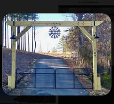 an open gate with a windmill in the background on a dirt road surrounded by trees