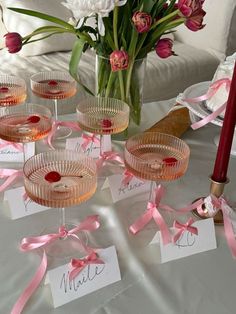 there are wine glasses on the table with pink ribbons around them and place cards in front of them