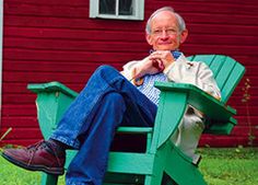 an older man sitting on a green chair in front of a red building and grass