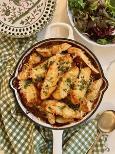 some food is sitting in a pan on a table next to a bowl of salad