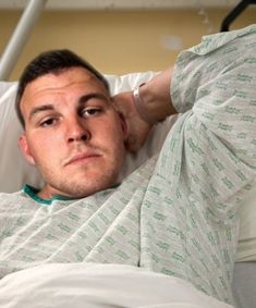 a man laying in a hospital bed with his hand on his head and looking at the camera