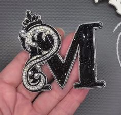 the letter m is made up of black and white crystals with a crown on top