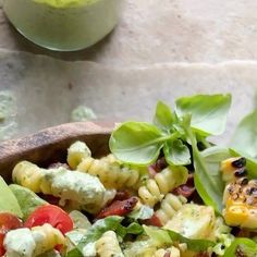 a wooden bowl filled with salad next to a glass of green liquid on top of a table