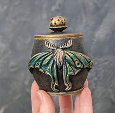 a hand holding a small ceramic jar with a butterfly on it