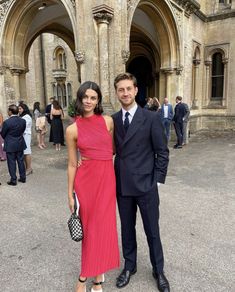 a man and woman standing in front of an old building wearing formal wear, smiling for the camera