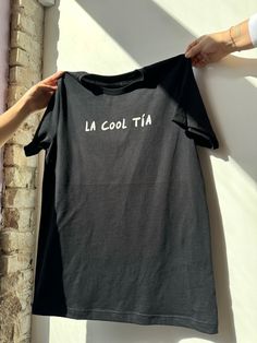 We all have that one cool tía... or you are the cool tía! Show all the Tías appreciation this Mother's Day for being great role models with this tee? *Don't forget to match your mini with our "Cool like my tía" kids tee* * Black tee/ White ink  * Unisex Fit  * Screen printed with love by JZD in Brownsville, TX * Made to order. Please allow 7-10 days. Our small but mighty team is pouring so much love in to these for all our tías. Cool Black Cotton T-shirt, Tan Cotton Crew Neck Top, Tan Cotton T-shirt With Text Print, Cool Cotton Graphic Print Top, Cool Cotton Tops With Graphic Print, Cool Cotton Slogan T-shirt, Casual Cotton Slogan Tops, Cotton Tops With Text Print, Cool Slogan Tops For Summer