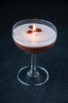 a candle is lit on top of a drink in a coupe glass filled with liquid