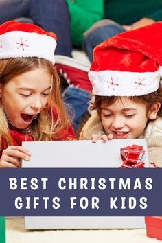 two girls in santa hats looking at a sign with the words best christmas gifts for kids