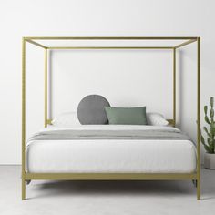 a white bed with a gold frame and pillows on it's headboard, next to a potted cacti