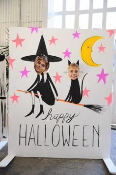 two children dressed up as witches on a happy halloween sign with the moon and stars behind them