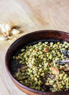 a wooden bowl filled with green beans and nuts on top of a table next to a spoon