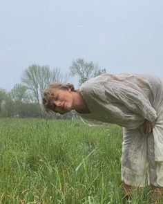 a woman standing in the middle of a field with her hands on her hips and head down