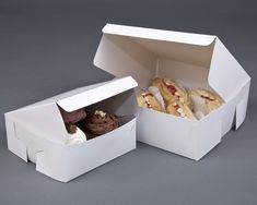 two white boxes with different types of pastries in them on a gray surface, one opened and the other closed