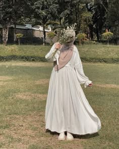 a woman in a white dress is walking through the grass with flowers on her head