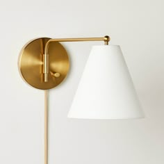 a gold wall light with a white shade on the side and a wooden stick next to it