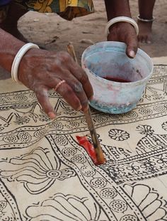 a woman is painting on the ground with her hand and knife in front of a bowl