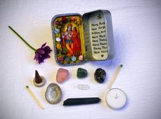 an open tin with some rocks and candles in it next to a flower on a table