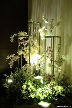 an arrangement of white flowers and greenery on display in front of a curtained window