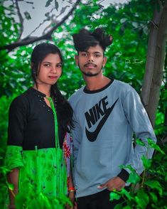 a man and woman standing next to each other in front of some trees with green leaves