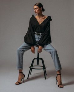 a woman sitting on top of a stool wearing high heeled sandals and a black shirt