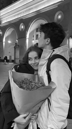 a man and woman standing next to each other holding a bouquet of flowers in front of a building