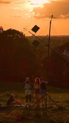 three people are standing in the grass near a radio antenna and some trees at sunset