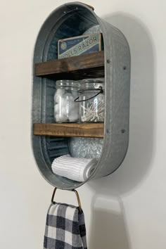 an old metal wall shelf with jars and towels hanging from it's sides on a white wall