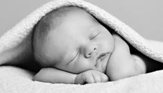 a black and white photo of a sleeping baby wrapped in a blanket with his eyes closed