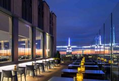 an outdoor restaurant with tables and chairs overlooking the city skyline at night, lit up by bright lights