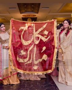 two women standing next to each other holding a large banner that says she is in arabic