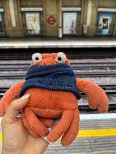 a hand holding an orange stuffed animal with googly eyes and a blue scarf around it's head