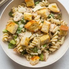 a white bowl filled with pasta and chicken salad next to chopsticks on the side