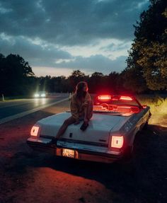 a woman sitting on the hood of a white car in front of a red light