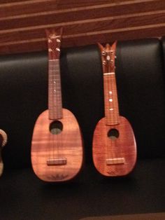 three ukulele sit side by side on a black bench next to a teddy bear