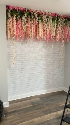 a ladder is in front of a white brick wall with pink and green flowers hanging from it