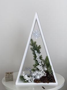 a triangle shaped christmas decoration with pine cones, balls and other decorations on a white table