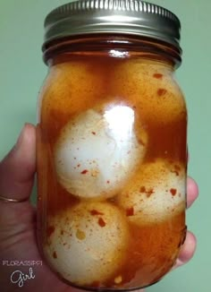 a hand holding a mason jar filled with some kind of liquid and eggs in it