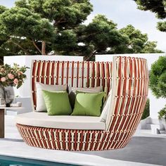 an outdoor daybed with pillows and green cushions next to a swimming pool, surrounded by greenery